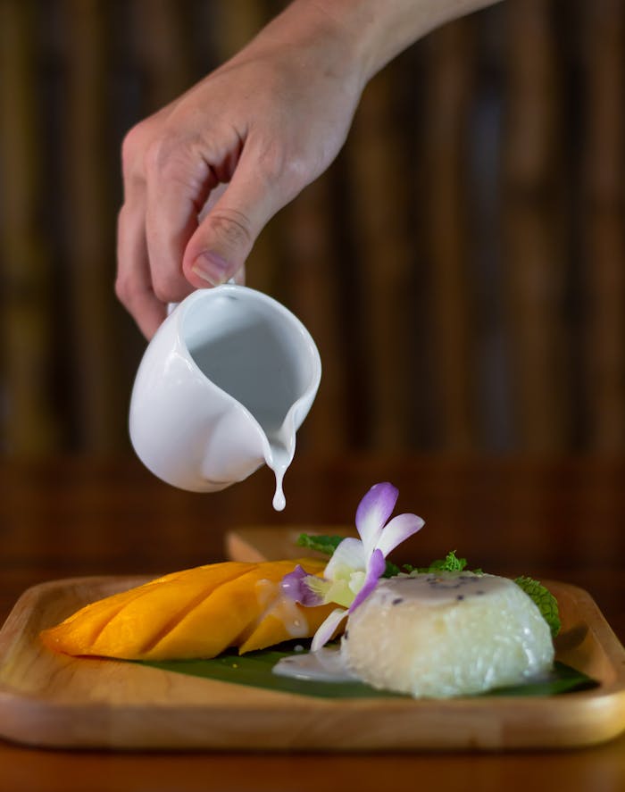 Traditional Thai sticky mango rice dessert being prepared with coconut milk drizzle. A delightful treat.